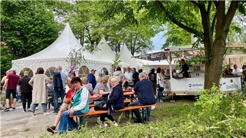 Menschen sitzen und stehen vor einem Festzelt. 