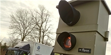 Rechts im Bild ist ein stationärer Blitzer zu sehen, links daneben ein Lkw.