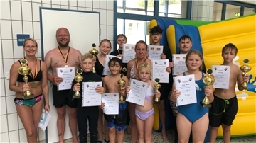 Gruppe von Menschen mit Pokalen und Urkunden im Schwimmbad.