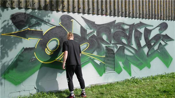 Ein Mann sprüht ein Graffiti an eine Wand.