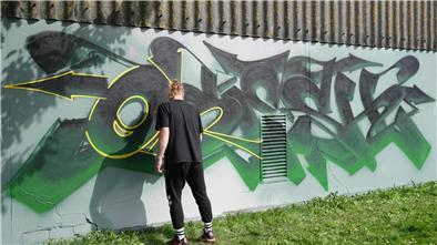 Ein Mann sprüht ein Graffiti an eine Wand.