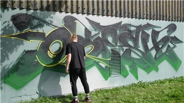 Ein Mann sprüht ein Graffiti an eine Wand.
