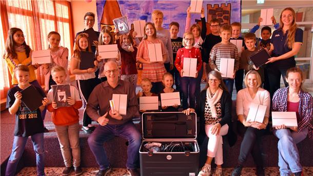 Eine Schulklasse und ihre Lehrer freuen sich über neue iPads.