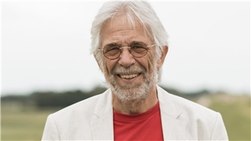 Älterer Mann mit Brille in einem hellen Jackett. 