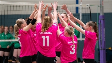 Eine Gruppe junger Frauen steht vor einem Volleyballnetz und jubelt gemeinsam. 