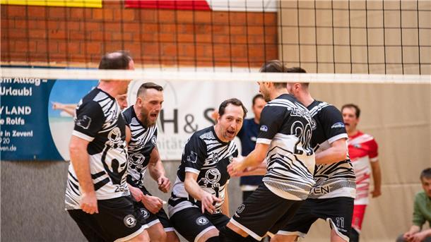 Männer hinter einem Volleyballnetz, die gemeinsam jubeln. 