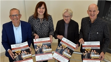Zwei Männer und zwei Frauen halten ein Plakat mit einer Konzertankündigung in die Kamera und lächeln