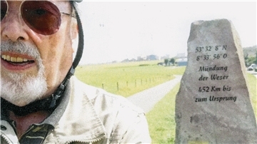 Rentner mit Sonnenbrille und Fahrradhelm fotografiert sich selbst vor dem Weserstein in Nordenham-Blexen.