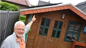 Ein Mann zeigt auf das Dach seines Gartenhäuschens, auf dem ein Balkonkraftwerk installiert ist.