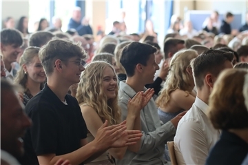 Junge Menschen sitzen dicht an dicht, lachen und klatschen in die Hände.