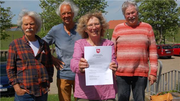 Drei Männer und eine Frau stehen lächelnd vor der Kamera. Die Frau hält einen Brief vom Land Niedersachsen in die Kamera.