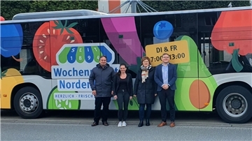 Vier Leute stehen vor einem großflächig beklebten Linienbus.