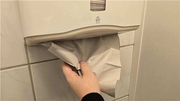 Eine Hand greift nach Papierhandtüchern in einem Spender