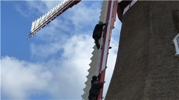 Handwerker erklimmen die Mühle, um ein Windbrett nach dem anderen einzusetzen. Jetzt sind die Jalousienflügel wieder komplett.