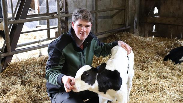 Zwei „Kuhmenschen“ starten mit Stipendium durch Mann im Kuhstall mit Stroh und Kalb. Hannes Tramm kümmert sich um ein Kalb.