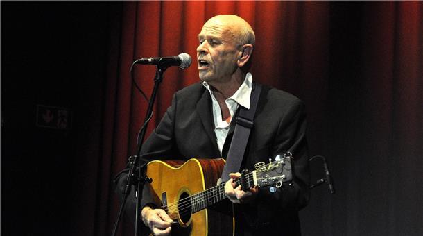 Mann mit Gitarre steht an einem Mikrofon und singt.
