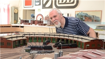 Ein Mann sitzt vor einer Modelleisenbahn.
