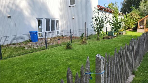 Hier entstehen in Nordenham 15 neue Kita-Plätze Eine eingezäunte Rasenfläche vor einer weißen Halle.