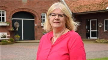 Frau steht im roten Hemd vor ihrem Hof.