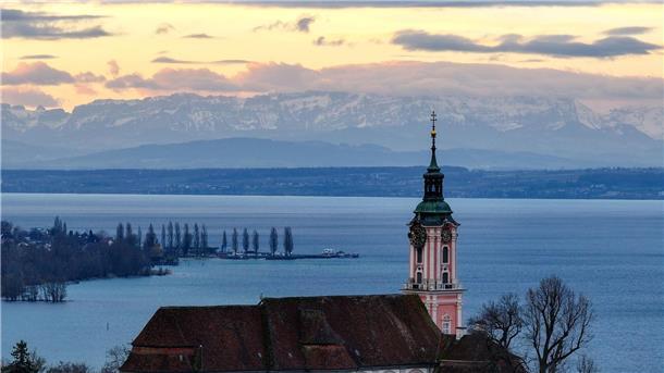 Bis zu 18 Grad am Samstag in Süddeutschland Hinter der ehemaligen Klosterkirche Birnau am Bodensee geht die Sonne auf. Die Alpen sind im Hintergrund zu sehen.