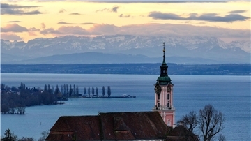 Hinter der ehemaligen Klosterkirche Birnau am Bodensee geht die Sonne auf. Die Alpen sind im Hintergrund zu sehen.