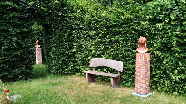 Ein Garten, in dem unter anderem eine Bank vor einer Hecke steht. Und zwei Skulpturen sind zu sehen. Hinter hohen Hecken verborgen lädt der Garten der Epikurike in Nartum mit Skulpturen, seltenem Baumbestand und stillen Ecken zum Verweilen und Entdecken ein.