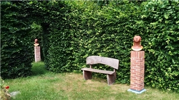 Ein Garten, in dem unter anderem eine Bank vor einer Hecke steht. Und zwei Skulpturen sind zu sehen. Hinter hohen Hecken verborgen lädt der Garten der Epikurike in Nartum mit Skulpturen, seltenem Baumbestand und stillen Ecken zum Verweilen und Entdecken ein.