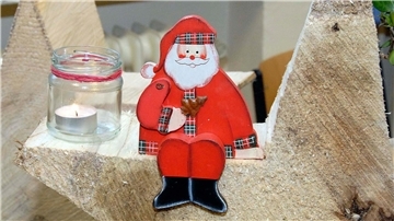Ein Weihnachtsmann aus Holz sitzt neben einem Glas mit einer Kerze.