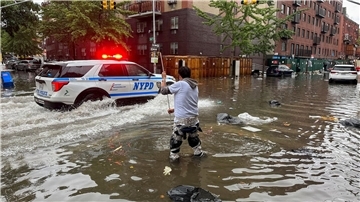 Hochwasser auf den Straßen von New York: Im Stadtteil Brooklyn versucht ein Mann, mit einem  Stock einen Abfluss zu reinigen, während ein Polizeiwagen vorbeifährt.