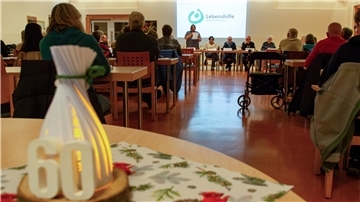 Menschen sitzen auf Stühlen und hören einer Gruppe Menschen zu, die sich vor ihnen ebenfalls auf Stühlen sitzend befindet. 