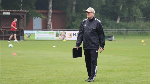 Fusion und Neuzugänge: SV Ippensen/Wohnste startet neu durch Ein Mann in einem schwarzen Sportdress und einer Cap hält eine Mappe in der Hand und geht über einen Rasen.