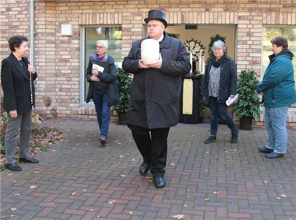 Mehrere Menschen vor einer Kapelle Bestatter mit Urne in der Hand