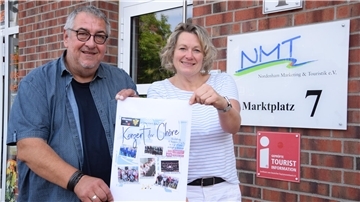 Ein Mann und eine Frau halten ein Plakat des Konzerts der Chöre in den Händen.