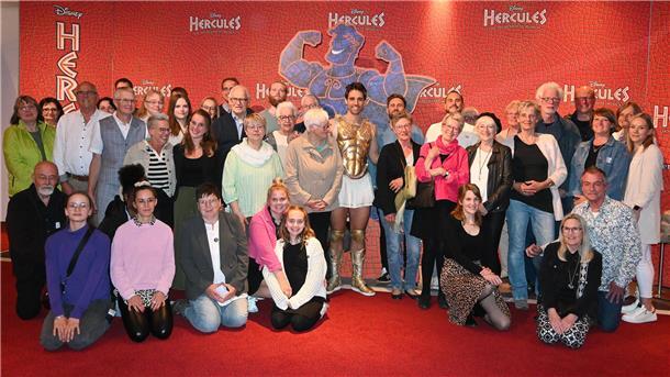 Rund 50 Menschen stehen als Gruppe beisammen. In der Mitte: ein Musicaldarsteller in Hercules-Kostüm.