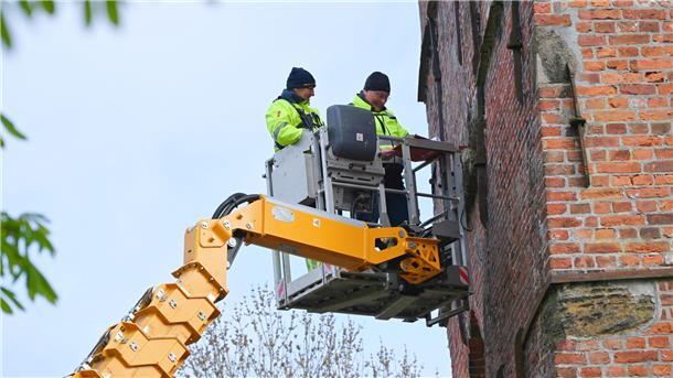 Zwei Männer, die auf einer Arbeitsbühne stehen, untersuchen von außen den Turm der Blexer Kirche.