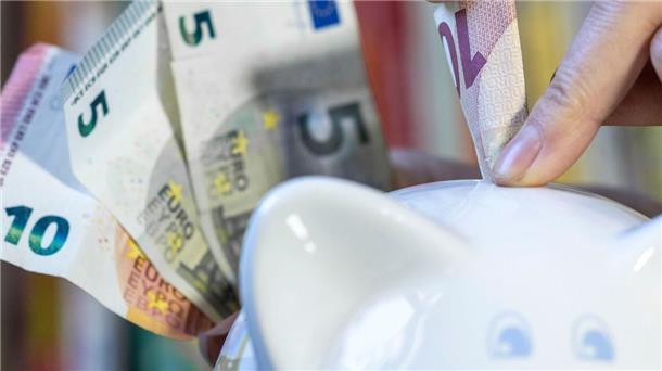 Bild von Euro-Scheinen, die eine Frauenhand in ein Sparschwein steckt