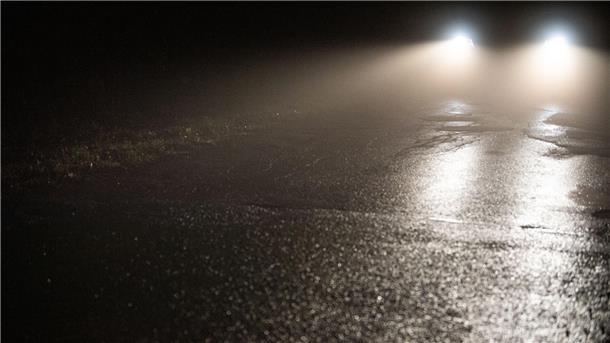 Scheinwerfer strahlen über nassen Asphalt.