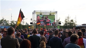 Es ist eine Leinwand zu sehen. Fußballfans stehen davor und fiebern mit. 