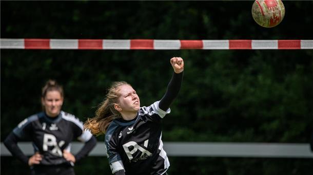Eine Frau schlägt einen Ball über ein rotweißes Band.