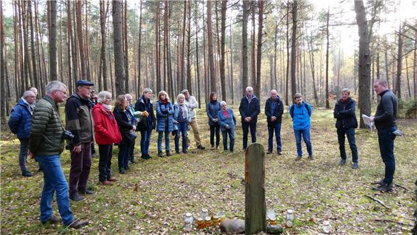 Im Wald bei Sobibor: Historiker Dr. Andreas Kahrs (rechts) und Freunde konnten hier die Hinrichtungsstätte von sechs jüdischen Häftlingen lokalisieren, die am 19. Oktober 1943 am Ende ihrer verzweifelten Flucht erschossen wurden. Die Teilnehmenden der Erkundungsfahrt des Gedenkstättenvereins Sandbostel versammeln sich schweigend im Halbkreis am Scheit, um an diesem Gedenkort Astern niederzulegen.
