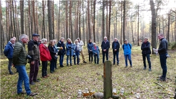 Im Wald bei Sobibor: Historiker Dr. Andreas Kahrs (rechts) und Freunde konnten hier die Hinrichtungsstätte von sechs jüdischen Häftlingen lokalisieren, die am 19. Oktober 1943 am Ende ihrer verzweifelten Flucht erschossen wurden. Die Teilnehmenden der Erkundungsfahrt des Gedenkstättenvereins Sandbostel versammeln sich schweigend im Halbkreis am Scheit, um an diesem Gedenkort Astern niederzulegen.