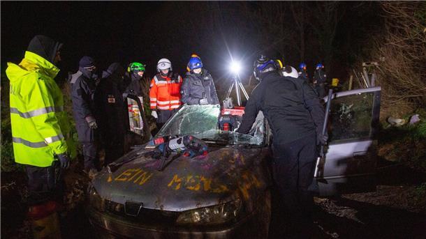 Abrissbagger in Lützerath - Widerstand bröckelt In dem Autowrack hat sich eine Aktivistin durch das Bodenblech in den darunterliegenden Weg mit den Füßen einzementiert.