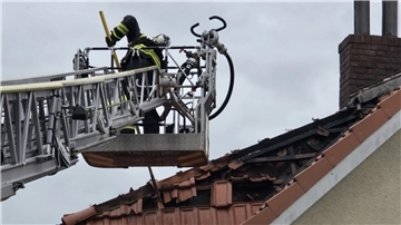 Ein Feuerwehrmann auf einer Drehleiter nimmt Dachziegel mit einem Stab ab.