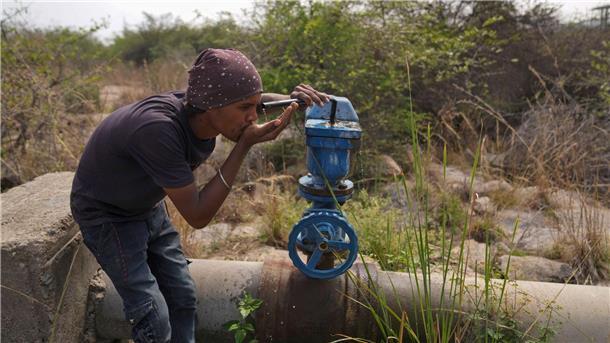 In Indien trinkt ein Mann Wasser aus einer undichten Wasserstelle.