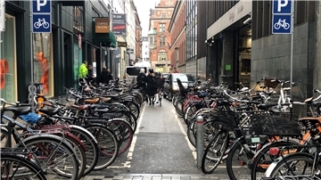 Zwei Frauen gehen mit ihren Fahrrädern an einem Fahrradparkplatz in der Kopenhagener Innenstadt vorbei.
