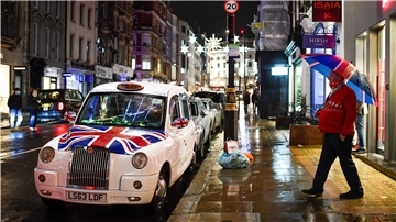 Ein Taxifahrer geht am Samstag im Londoner Stadtteil Mayfair mit einem Regenschirm in den Farben der Flagge von Großbritannien in der Hand zu seinem Taxi, auf dessen Motorhaube eine weitere Flagge des «Union Jack» prangt.