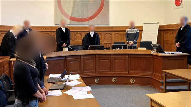 Ein Gerichtssaal zeigt acht Personen, davon eine Frau. Alle Gesichter sind gepixelt.