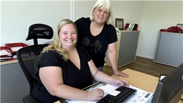 eine Frau steht neben einer anderen, die an einem Schreibtisch sitzt