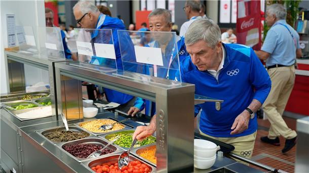 Trotz Kritik: „Wahrer Geist des Sports“ im olympischen Dorf IOC-Präsident Thomas Back kostet vom Essen im Olympischen Dorf.