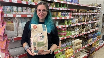 Eine Frau steht vor einem Regal mit Tierfutter. In den Händen hält sie einen Sack Hundefutter.